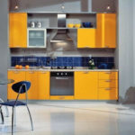 Krāsu kombinācija oranžā un tumši zilā virtuves interjerā uz pelēka fona