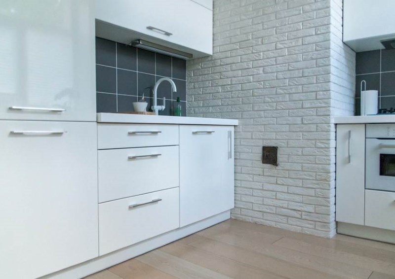 Минималистичен бял кухненски интериор с тухлена стена