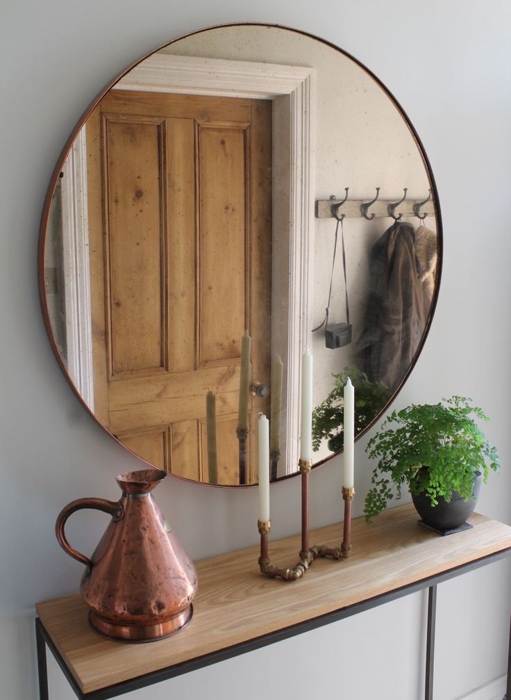 A round mirror in a thin frame opposite a wooden door