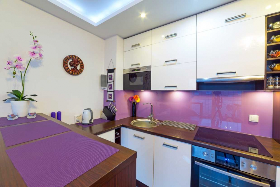 Dulapuri albe peste un șorț lila într-o bucătărie mică