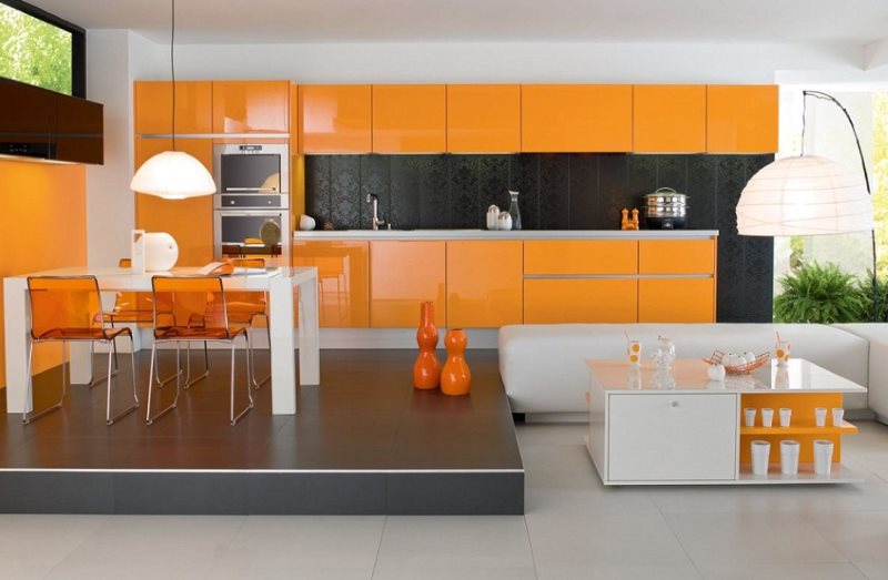Oranža virtuve ar ēdamistabas zonu uz pjedestāla.