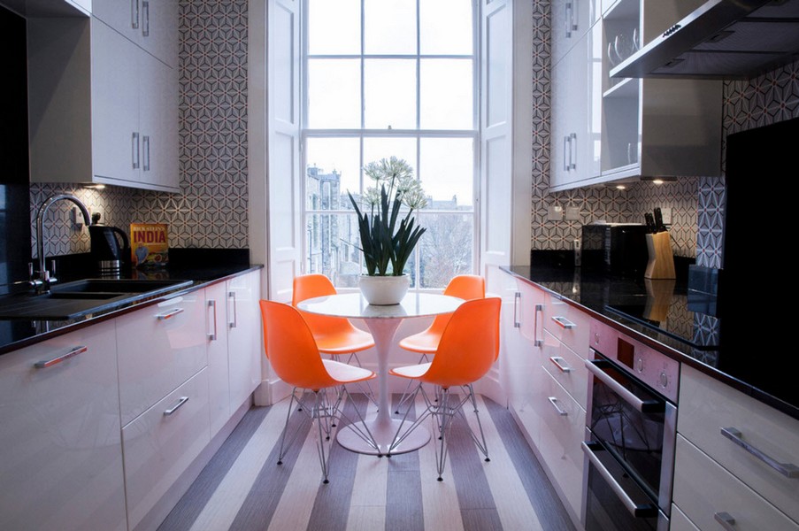 Oranžie krēsli šaurā paralēlā virtuvē