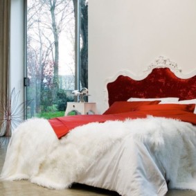 Sarkans gultas pārklājs uz baltas gultas