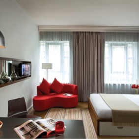 Sarkans dīvāns viesistabā ar diviem logiem