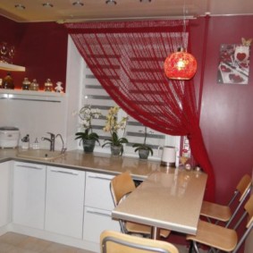 Punainen verho keittiön ikkunassa valkoisilla huonekaluilla