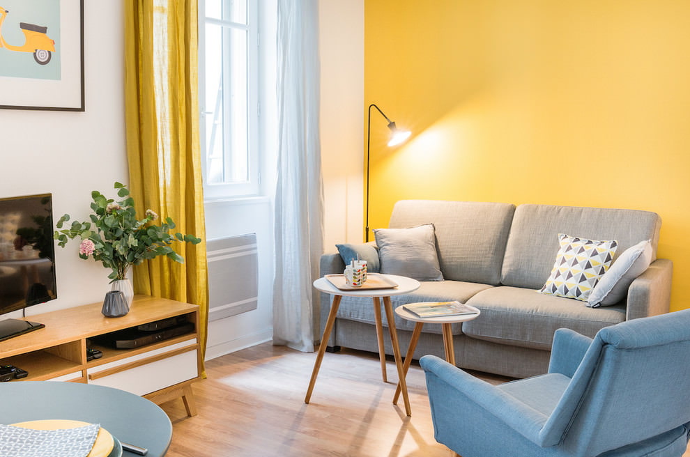Pelēks dīvāns uz viesistabas dzeltenās sienas fona