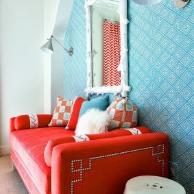 Sarkans dīvāns zālē ar zilām tapetēm