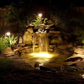Garden lights on the shore of a pond with a waterfall
