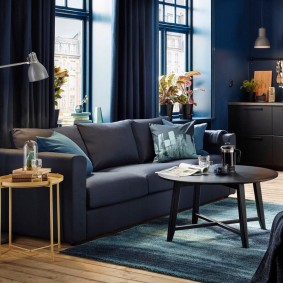 Saliekams dīvāns zālē ar ziliem aizkariem