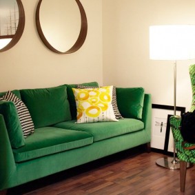 Spoguļa sienas dekors virs zaļa dīvāna
